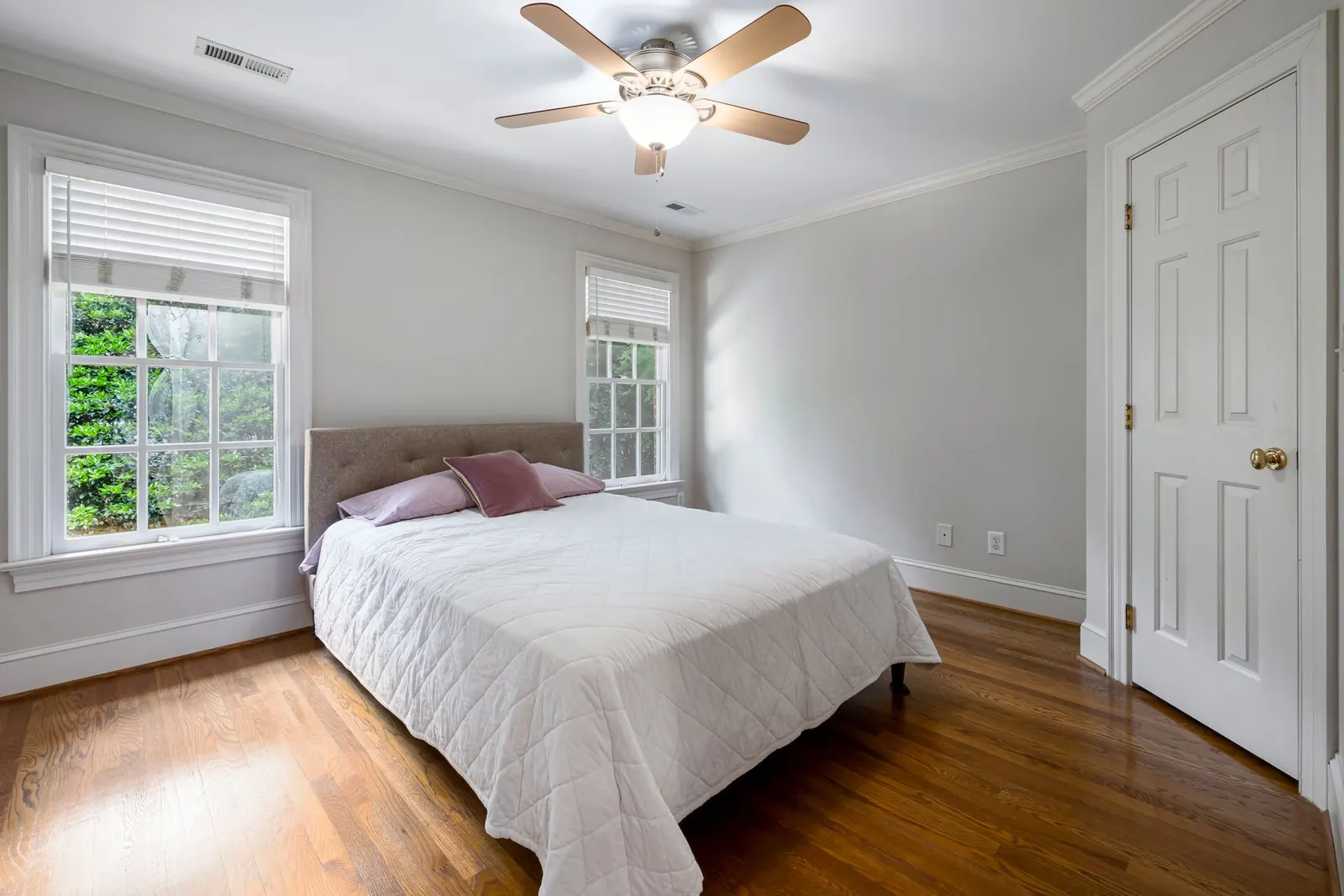 Bedroom with a white quilt, hardwood floor and ceiling fan in daylight