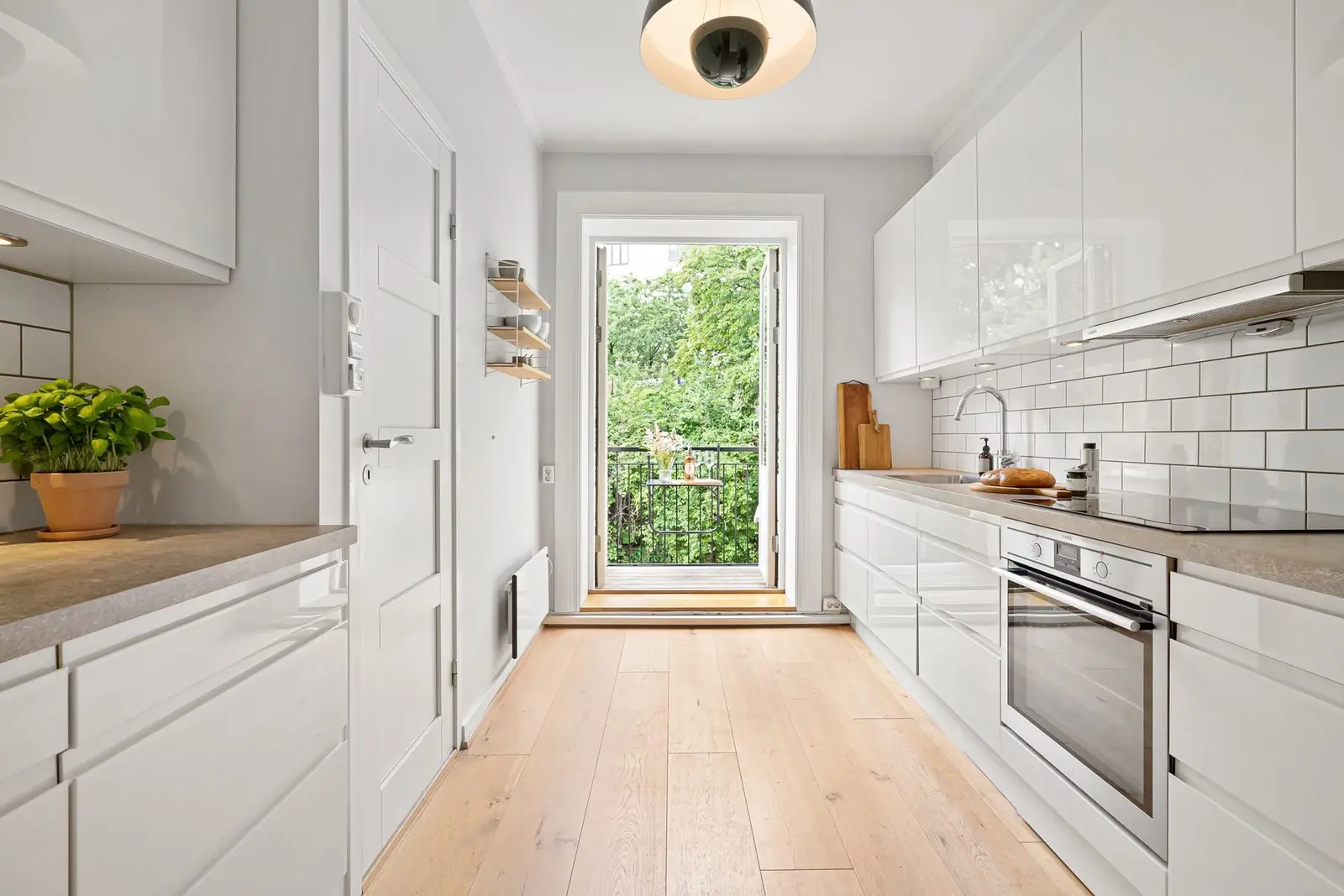 Compact white galley kitchen with a light wood floor and a balcony door