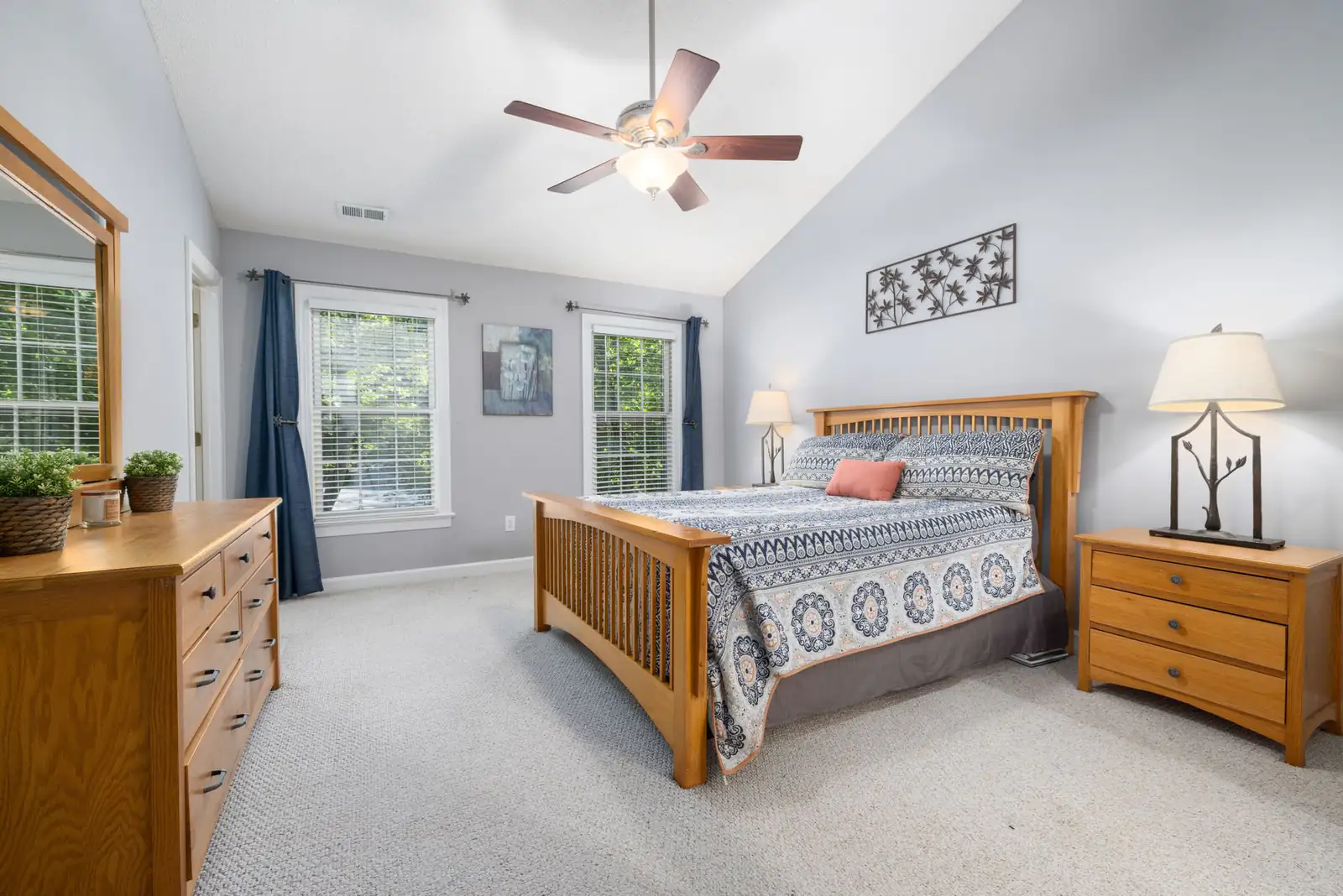 Carpeted main bedroom with an oak bed, dresser, blue curtains and a vaulted ceiling