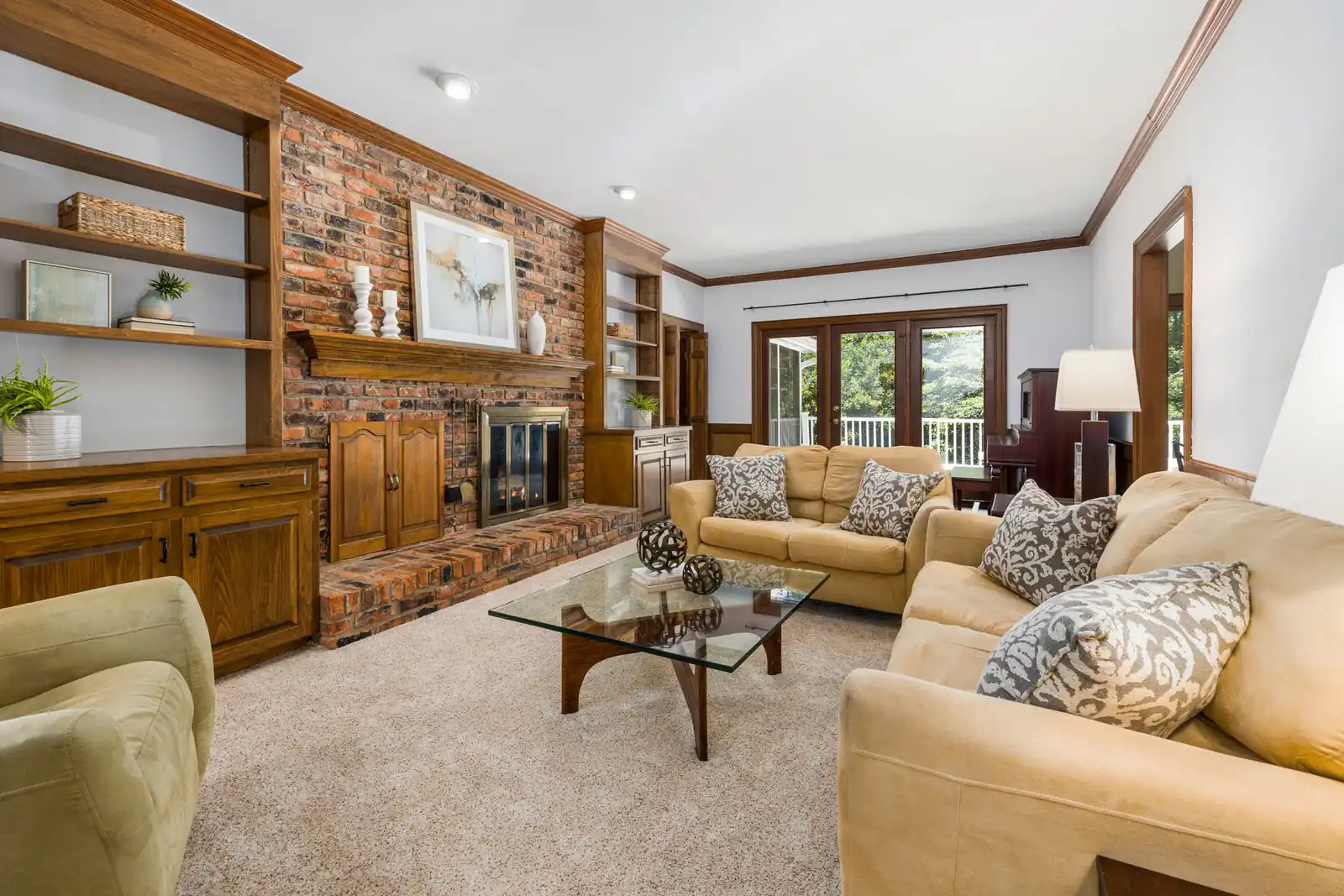 Carpeted family room with a brick fireplace, oak built-ins and tan sofas