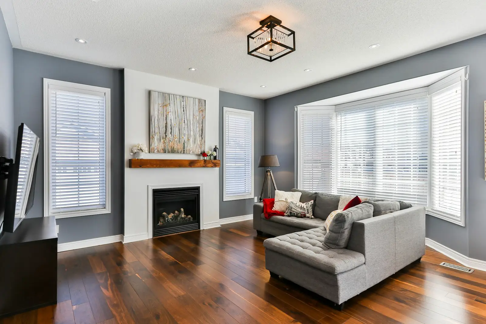 Grey-walled living room with a sectional, gas fireplace, bay window and hardwood floor